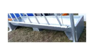 Metalowy żłób na paszę, stojący na trawie, gotowy do karmienia zwierząt.