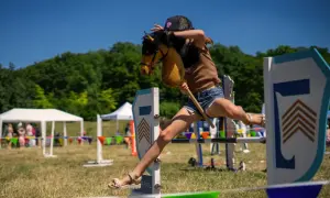 Dziewczynka na kucyku z patyka przeskakuje przez przeszkodę. Czy hobby horse to sport? Z pewnością wymaga zwinności i determinacji!