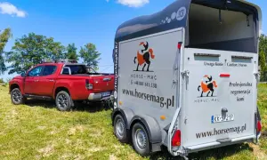 Czerwony pickup holuje przyczepę do przewozu koni. Na przyczepie logo Horse-Mag i napis "Uwaga Konie".