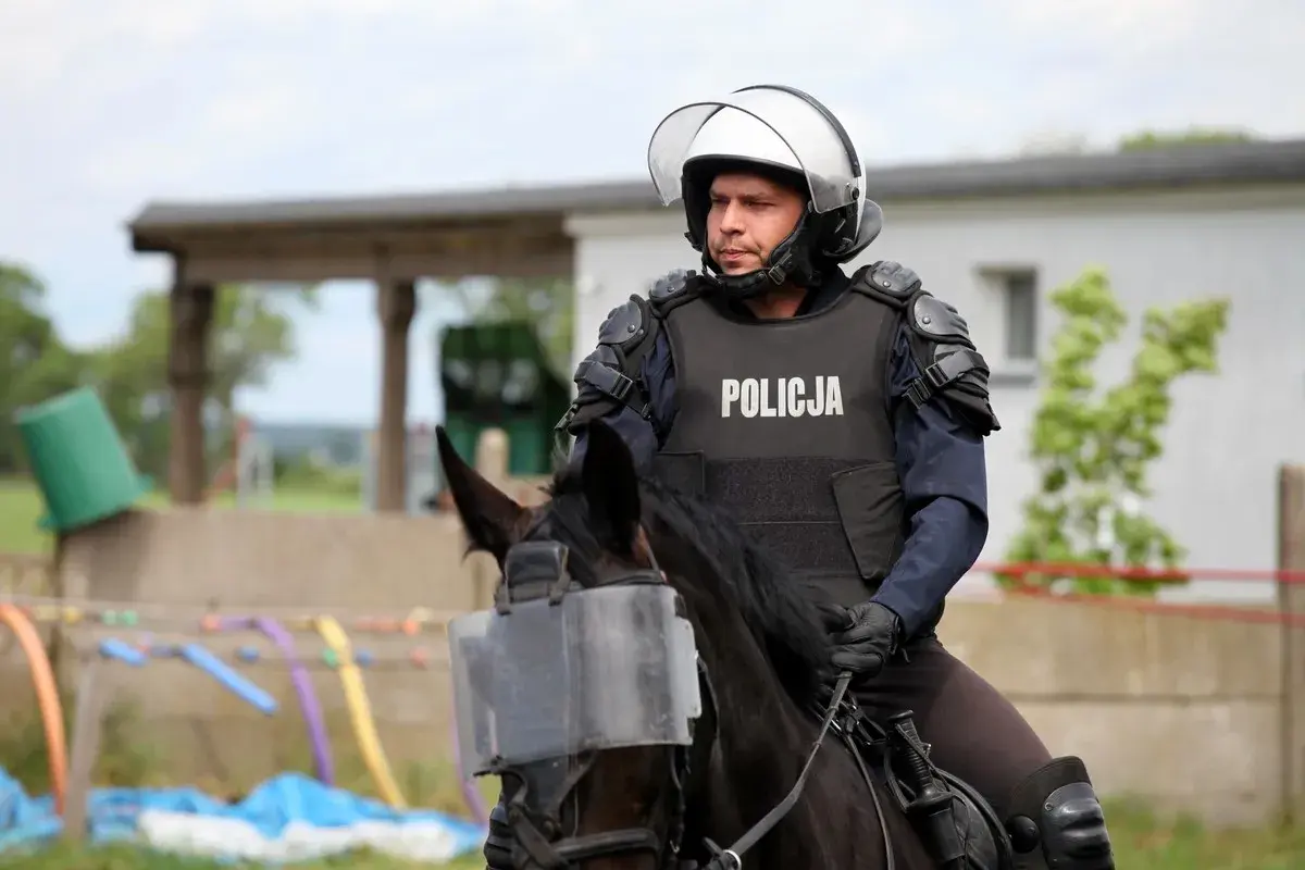 Policjant w pełnym rynsztunku, na koniu z osłoną na pysk, gotowy do akcji. Konie policyjne to ważny element służby.