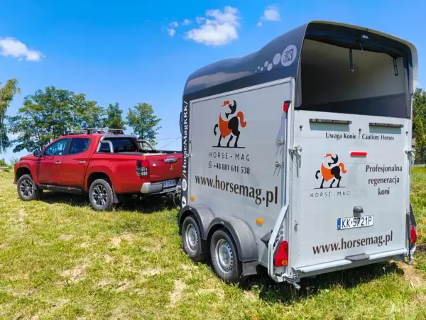Czerwony pickup holuje przyczepę do przewozu koni. Na przyczepie logo Horse-Mag i napis "Uwaga Konie".